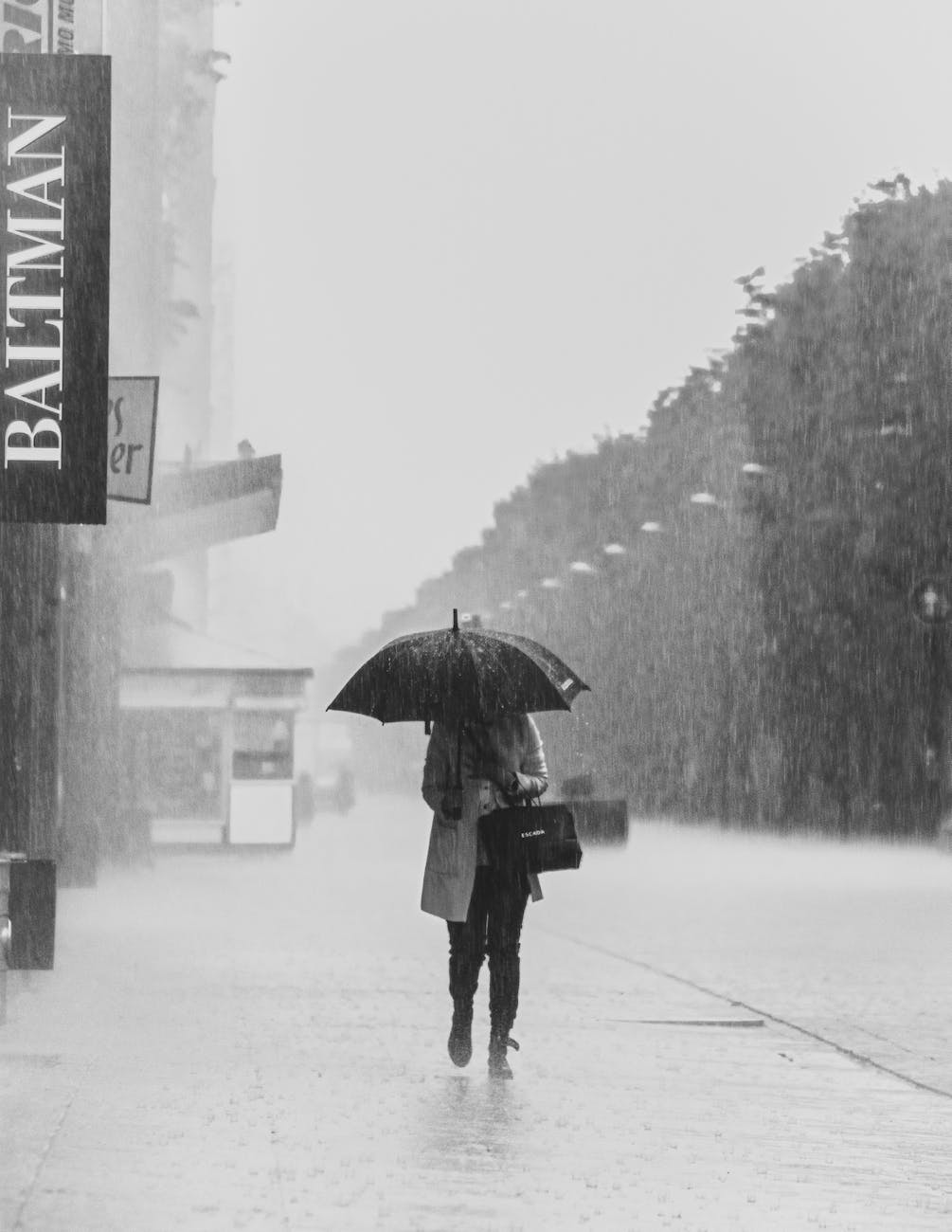grayscale photo of a person holding an umbrella while walking on the street